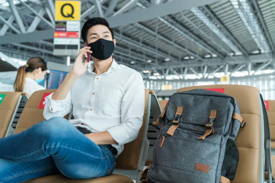 איש יושב בשדה התעופה עם מסיכה על הפנים קונספט השפעת הקורונה על שדה התעופה